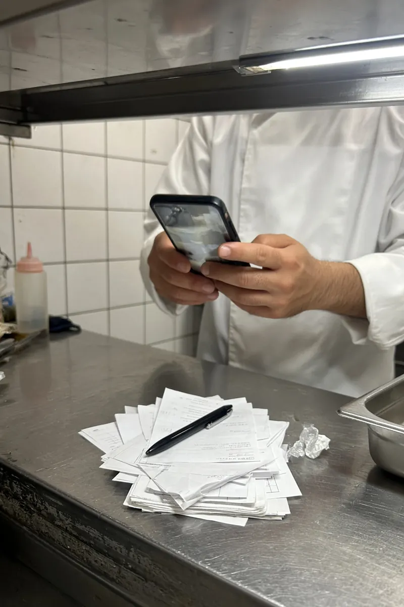 Mani di un cuoco con lo smartphone al pass della cucina, foto da telefono