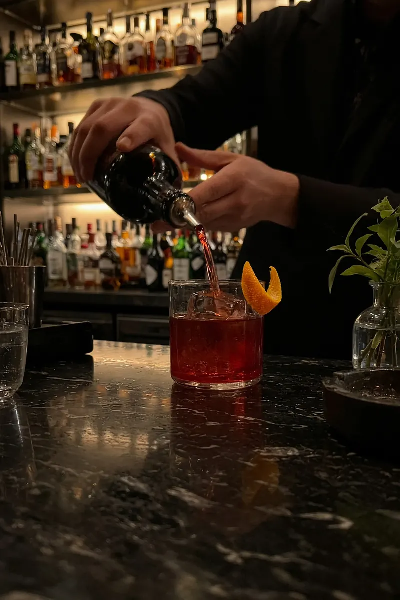 Barman che versa un negroni su ghiaccio al bancone